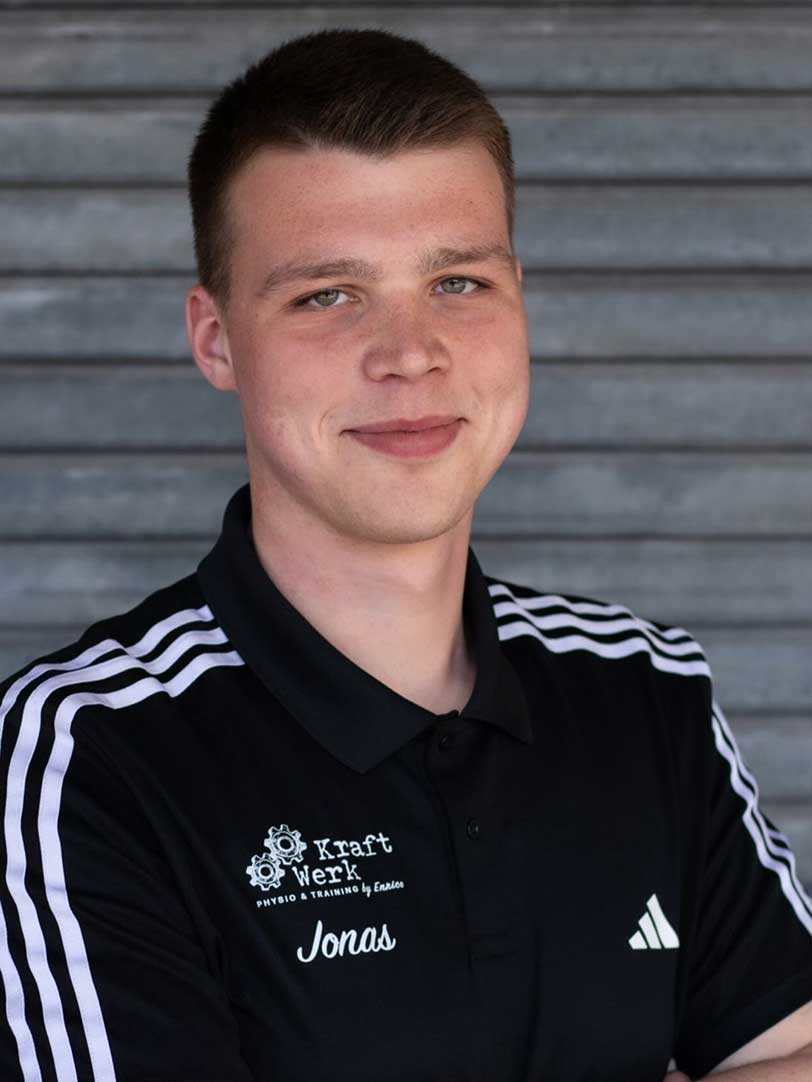 Ein junger Mann lächelt in schwarzem Adidas-Poloshirt mit weißen Streifen.