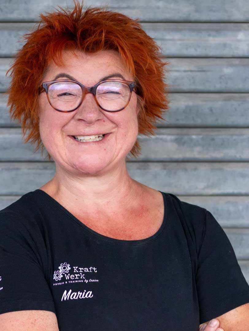Eine Frau mit roten Haaren lächelt fröhlich vor einer grauen Metalltür.