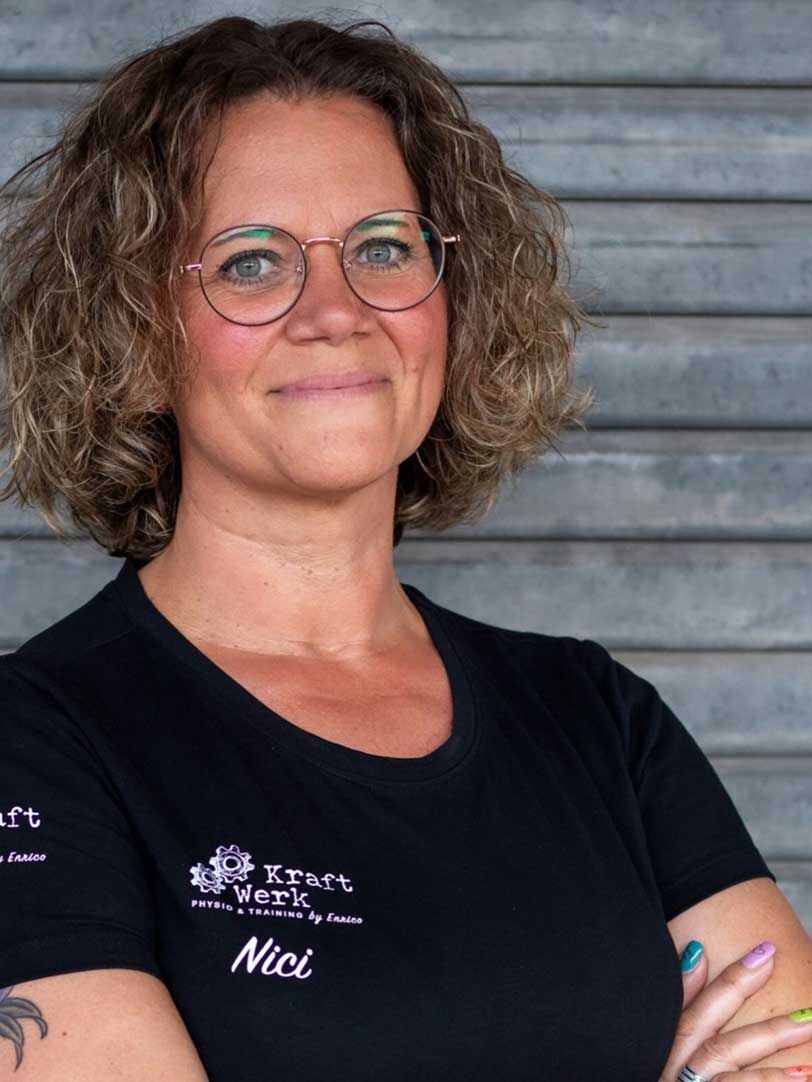 Eine Frau mit lockigem Haar und Brille lächelt und trägt ein schwarzes T-Shirt.