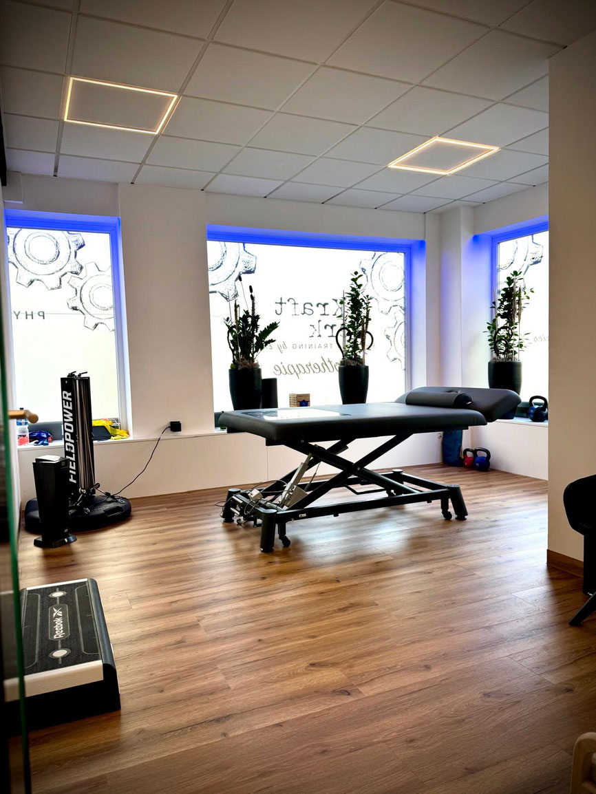 Heller moderner Therapieraum mit Massageliege, Holzfußboden und großen Pflanzen